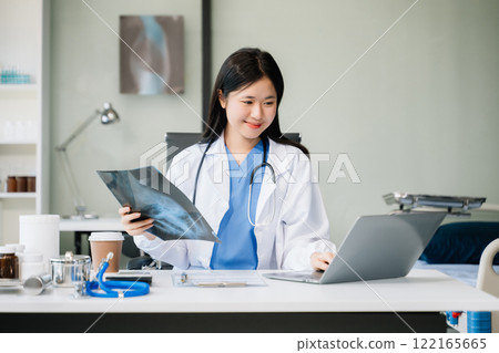 Confident young  female doctor in white medical uniform sit at desk working on computer. Smiling use laptop 122165665