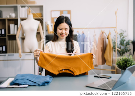 Asian young woman on desk in office of fashion designer and holds tablet, laptop and smartphone on desk Asian young woman on desk in office of fashion designer and holds tablet, laptop and smartphone on desk 122165735