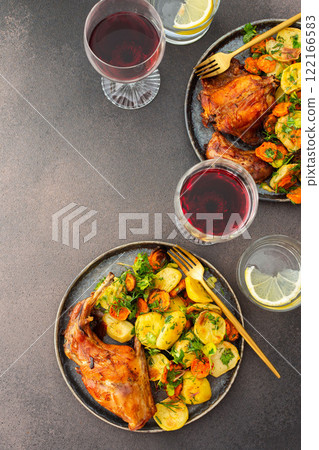 Baked rabbit with potatoes and carrots, a set table with food, a glass of wine and a vase of flowers Baked rabbit with potatoes and carrots, a set table with food, a glass of wine and a vase of flowers 122166583