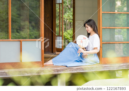 一位年輕女子坐在古民居的門廊上，用扇子搧風降溫 122167893