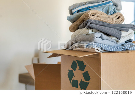 Pile of clothes in cardboard box donating for recycling reusing at living room with houseplant Pile of clothes in cardboard box donating for recycling reusing at living room with houseplant 122168019