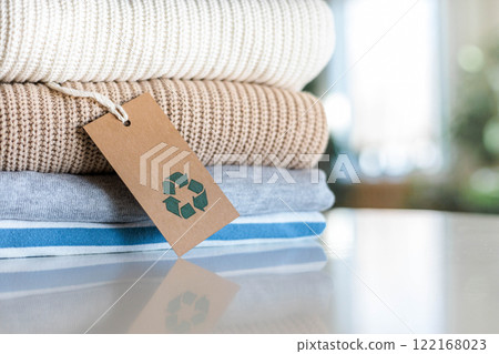 Knitted warm clothes neatly folded heap with craft tag recycling material circle arrow closeup Knitted warm clothes neatly folded heap with craft tag recycling material circle arrow closeup 122168023