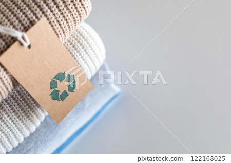 Knitted warm clothes neatly folded heap with craft tag recycling material circle arrow closeup Knitted warm clothes neatly folded heap with craft tag recycling material circle arrow closeup 122168025