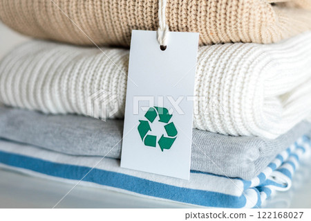 Knitted warm clothes neatly folded heap with craft tag recycling material circle arrow closeup Knitted warm clothes neatly folded heap with craft tag recycling material circle arrow closeup 122168027
