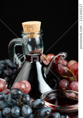 Red wine vinegar in glass vinegar bowl cruet among grapes 122168227