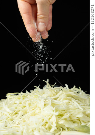 Sprinkling salt on chopped white cabbage, black background Sprinkling salt on chopped white cabbage, black background 122168271