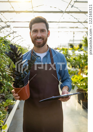 Young bearded man holding a potted flower and looking contented Young bearded man holding a potted flower and looking contented 122168321