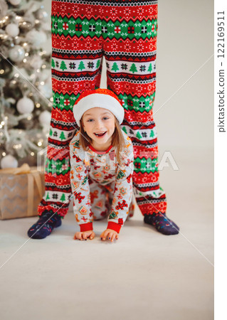Funny girl in pajamas and hat crawling between daddy's legs. new year holiday Funny girl in pajamas and hat crawling between daddy's legs. new year holiday 122169511