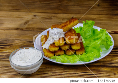 Fried fish fingers on a plate with lettuce and tartar sauce on wooden table Fried fish fingers on a plate with lettuce and tartar sauce on wooden table 122170956