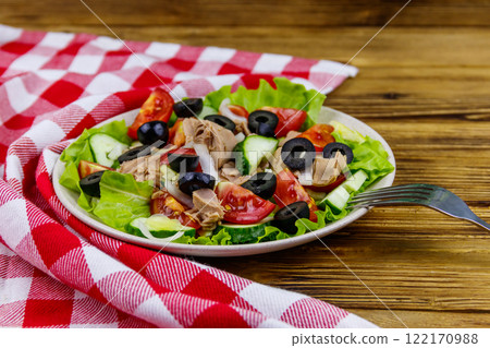 Tasty tuna salad with lettuce, black olives and fresh vegetables on wooden table 122170988