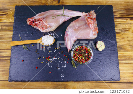 Raw rabbit legs with spices on a black slate cutting board on wooden table. Top view Raw rabbit legs with spices on a black slate cutting board on wooden table. Top view 122171082