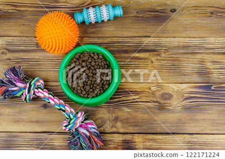 Dog toys and feed for dogs in green plastic bowl on wooden background. Top view. Dog care concept Dog toys and feed for dogs in green plastic bowl on wooden background. Top view. Dog care concept 122171224
