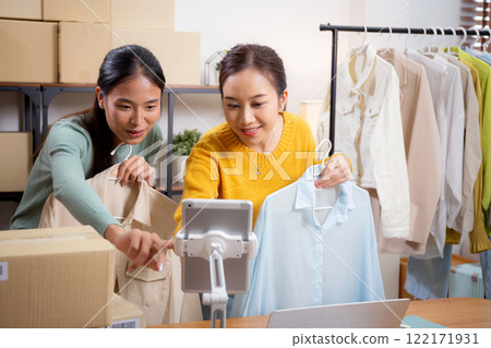 Two young asian woman live online clothing store while showing clothing with tablet on social. 122171931