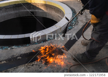 An industrial worker uses fire to soften a rubber underlay for floor insulation, showcasing precision and skill in a critical step of the construction process 122171958