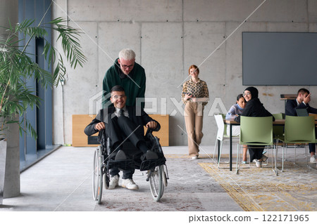 A diverse team of business colleagues, including a director in a wheelchair, engages in a collaborative discussion as they move together through a modern office space 122171965