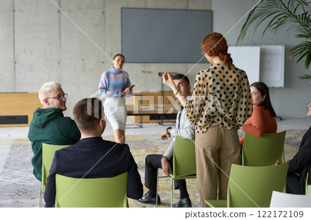 A diverse group of business professionals sits attentively in a modern office, actively participating in a training session led by an instructor, focusing on the latest technological advancements in 122172109