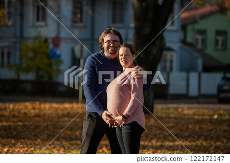 A man lovingly embraces his pregnant wife in the park, sharing a peaceful moment of warmth and affection A man lovingly embraces his pregnant wife in the park, sharing a peaceful moment of warmth and affection 122172147