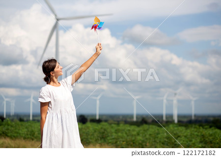 Young caucasian woman holding pinwheel in wind farm with turbines in blue sky nature. 122172182