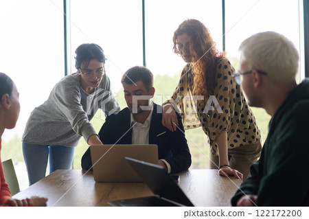 A diverse team of business professionals, along with the company director, reviewing business successes on a laptop in a modern office, discussing strategy and progress 122172200