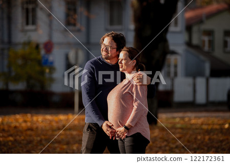 A man lovingly embraces his pregnant wife in the park, sharing a peaceful moment of warmth and affection  122172361