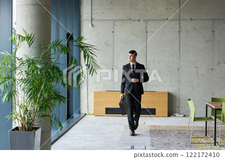 A determined businessman in a black suit confidently walks through the office, embodying professionalism and focus as he heads towards new challenges A determined businessman in a black suit confidently walks through the office, embodying professionalism and focus as he heads towards new challenges 122172410