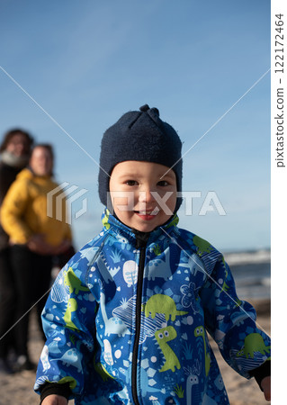 A happy family strolls along a chilly autumn beach, with their young son joyfully running ahead, creating lasting memories as the crisp wind and soothing waves embrace them in a moment of pure 122172464
