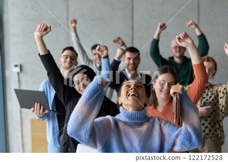 A diverse team of business professionals ecstatically celebrating their success in a modern office, expressing triumph and unity after achieving their goals 122172528