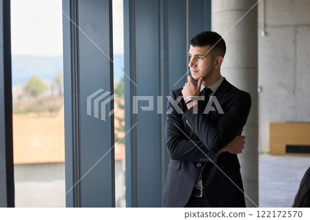 A close up portrait of a company director in a black suit, standing confidently in a modern office, exuding leadership, professionalism, and authority. 122172570
