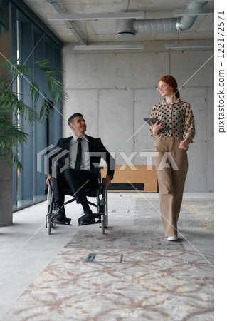 Director in a Wheelchair Navigating the Office While Discussing Business Challenges with a Colleague 122172571