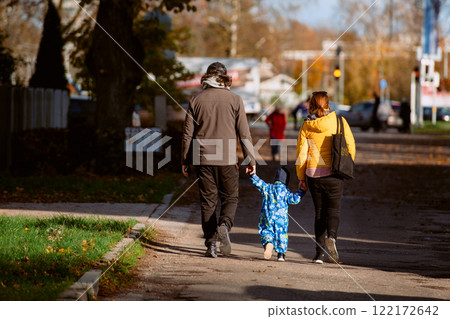 A loving couple strolls through a sunlit park with their young son, surrounded by the vibrant colors of autumn, enjoying a joyful and peaceful family moment together. 122172642