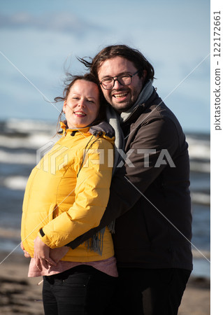 A couple stands embraced on a sandy beach on a chilly autumn day, the serene ocean stretching behind them as they share a quiet moment of love and warmth amidst the cool breeze and peaceful A couple stands embraced on a sandy beach on a chilly autumn day, the serene ocean stretching behind them as they share a quiet moment of love and warmth amidst the cool breeze and peaceful 122172661
