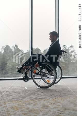 A businessman in a wheelchair enjoys a moment of laughter by a large window in a modern office, embodying positivity, resilience, and a balanced approach to work and life. A businessman in a wheelchair enjoys a moment of laughter by a large window in a modern office, embodying positivity, resilience, and a balanced approach to work and life. 122172713