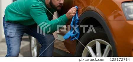 A man meticulously washes and cleans his car in the driveway of his home, showcasing pride in his vehicle and outdoor space. A man meticulously washes and cleans his car in the driveway of his home, showcasing pride in his vehicle and outdoor space. 122172714