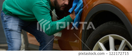 A man meticulously washes and cleans his car in the driveway of his home, showcasing pride in his vehicle and outdoor space. 122172715