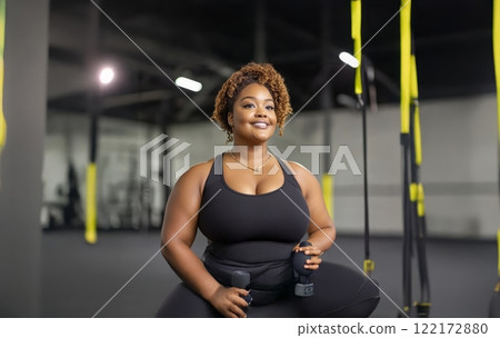 Plus size black woman in sportswear pushing through a workout at the gym, sweat dripping from her focused face. Generated image 122172880