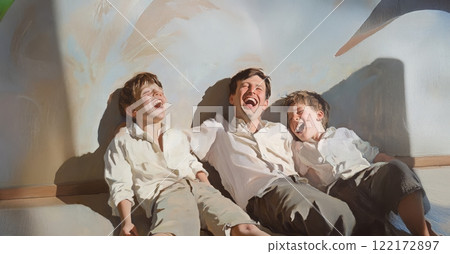 Father joyfully embracing his sons at home, lying on the floor and sharing laughter. Generated image 122172897