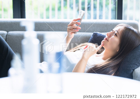 A woman lying on the sofa and using a smartphone A woman lying on the sofa and using a smartphone 122172972
