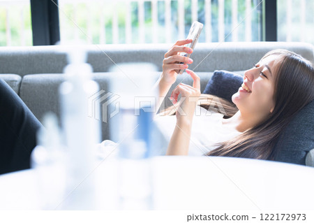 A woman lying on the sofa and using a smartphone A woman lying on the sofa and using a smartphone 122172973