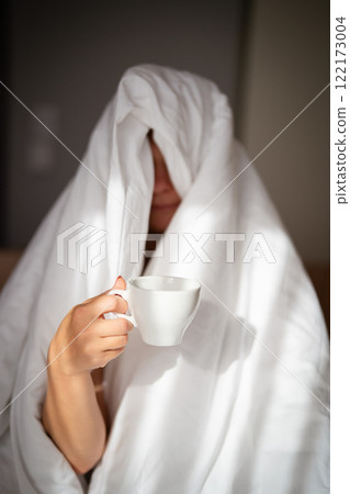 Woman with cup of coffee in the morning under the blanket at home 122173004