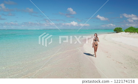 Young woman is walking on a pristine tropical beach with pink sand, turquoise water and lush vegetation in the maldives 122174158