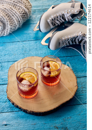 Two glasses of winter beverage with orange slices on wooden tray, ice skates and knitted blanket in background, reflecting festive and creative winter moments. 122174614