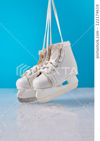 White ice skates hanging by laces against vibrant blue background, highlighting creative winter activities and seasonal joy. 122174619
