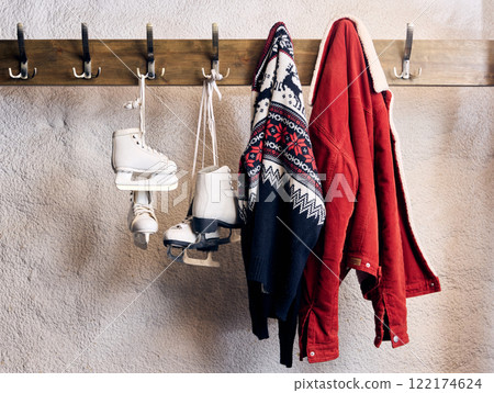 Winter wardrobe details including ice skates, patterned sweater, and festive red jacket hanging neatly, embodying holiday creativity and warmth. 122174624
