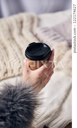 Hand holding cup of coffee with soft fur cuff in cozy setting, reflecting warm winter mornings and serene holiday moments. Hand holding cup of coffee with soft fur cuff in cozy setting, reflecting warm winter mornings and serene holiday moments. 122174627