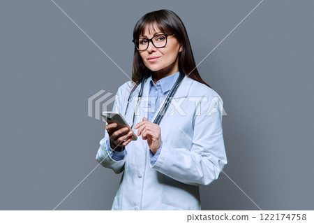 Portrait of female doctor holding smartphone on gray background Portrait of female doctor holding smartphone on gray background 122174758