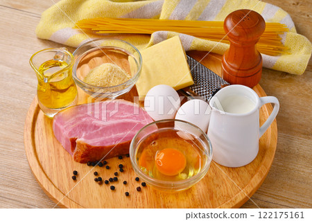 製作carbonara(義大利麵)菜餚的原料:雞蛋、培根、橄欖油、起司和牛奶。 製作carbonara(義大利麵)菜餚的原料:雞蛋、培根、橄欖油、起司和牛奶。 122175161