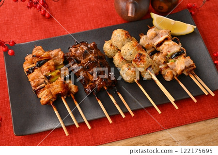 Yakitori (grilled chicken) dishes arranged on a long plate, garnished with sauce, salt, scallions, meatballs, liver, and lemon. 122175695