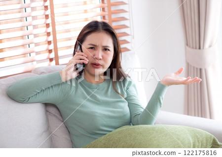 Asian young woman stress and worried sitting on sofa while speaking on smart phone in living room. 122175816