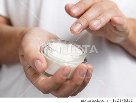 Woman touching cream with finger and holding a cosmetic jar in other hand, closeup Woman touching cream with finger and holding a cosmetic jar in other hand, closeup 122176331