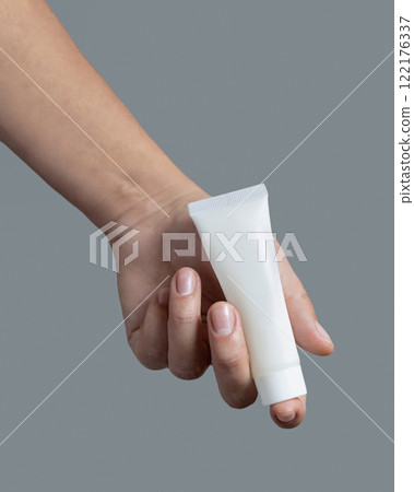 Female hand holding white cream tube against grey close up, cosmetic mockup, copy space 122176337